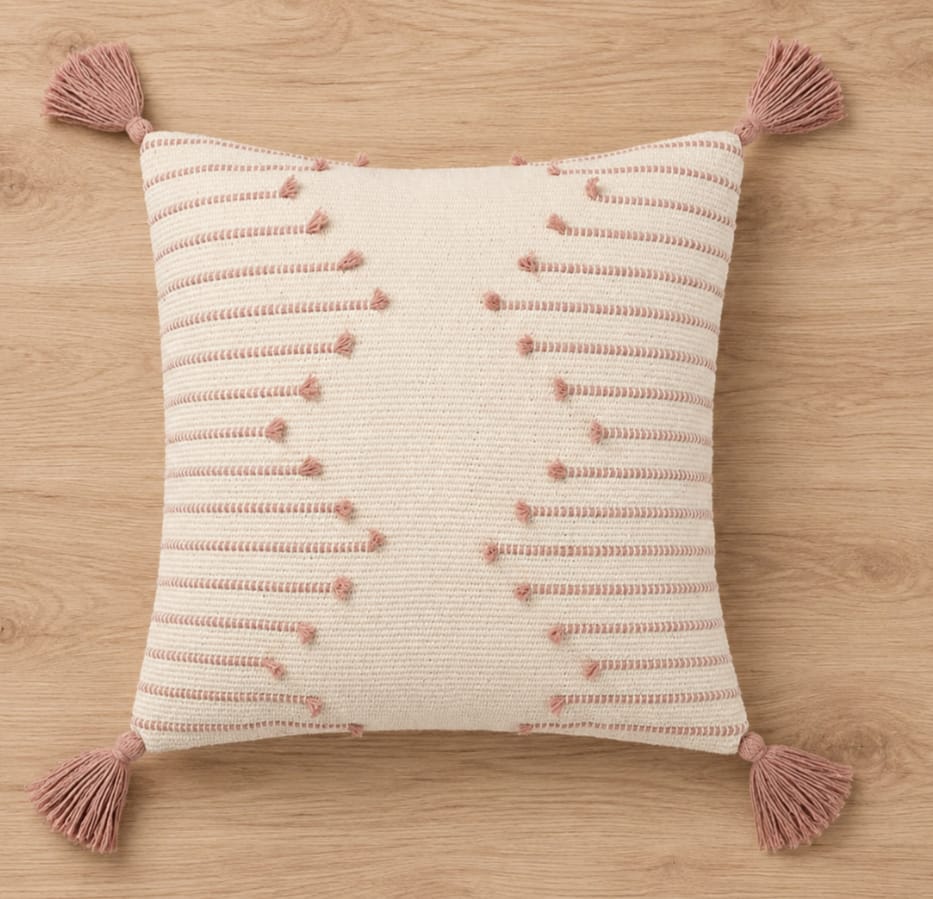 Handwoven ivory cotton cushion cover with blush pink stripes, textured tufted details, and decorative tassels, displayed on a wooden background.