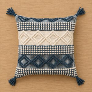 Handwoven blue and ivory boho cushion cover with geometric textured patterns and decorative tassels, displayed on a wooden background.